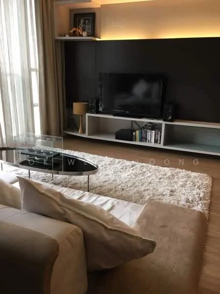 Living features: beige fabric sofa, glass coffee table, area rug with fluffy texture, wall-mounted TV, white shelving unit, dark accent wall, curtains in light beige, wooden flooring, decorative items on shelves; style: modern.