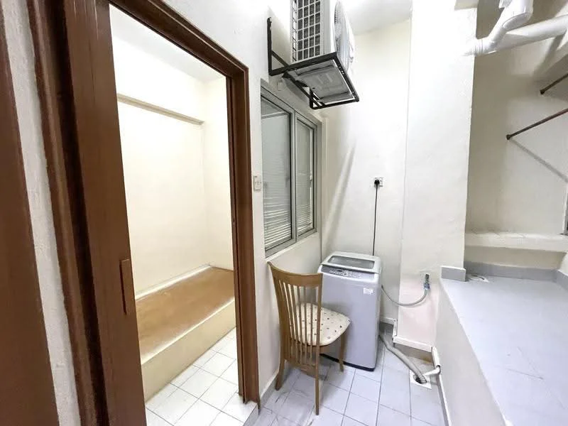 Laundry features: wall-mounted split AC, front-load washing machine, white tiled flooring, cream painted walls, window with blinds, corner countertop, staircase visible in background, chair. Room features: white painted walls, wooden door, step-up area.