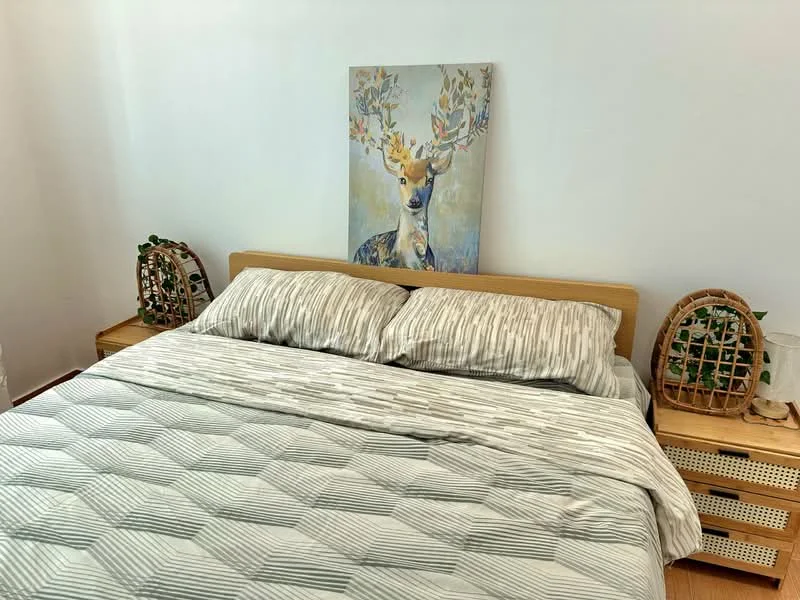 Bedroom features: king-size bed with striped bedding, wooden bed frame, framed artwork of a deer, two bedside tables, decorative plant on each bedside table, light-colored walls, wooden flooring, natural light from window; style: modern.