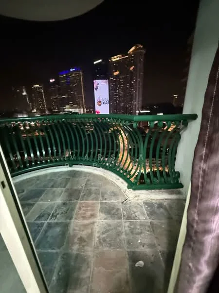 Room features: curved balcony, green wrought iron railing, stone flooring, city skyline view, nighttime lighting, visible high-rise buildings, outdoor space; view: city.