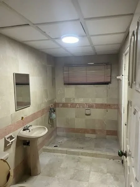 Bathroom features: white painted walls, light beige tile flooring, ceiling light fixture, mirror above sink, single-sink vanity with pedestal base, chrome faucet, toilet, window with blinds, pink accent tile border, exhaust fan, door with knob.