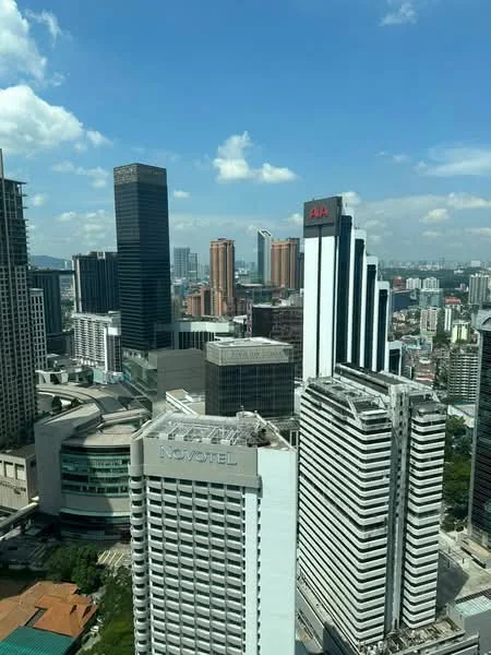 Exterior type: high-rise condominium; features: glass curtain wall, concrete facade, surrounded by city skyline, multiple high-rise buildings, urban landscape, visible commercial buildings, clear blue sky, clouds, adjacent to main road; style: modern.