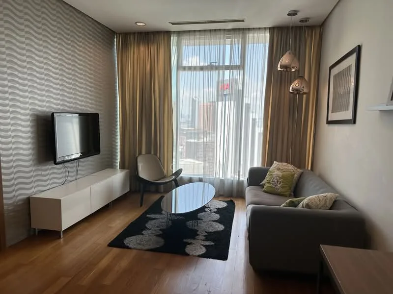 Living features: grey fabric sofa, 3-seater sofa, black area rug with geometric pattern, round coffee table, white TV console, wall-mounted TV, floor-to-ceiling windows, sheer curtains, wooden flooring, pendant lighting, decorative wall with wavy pattern, framed artwork; style: modern; view: city.