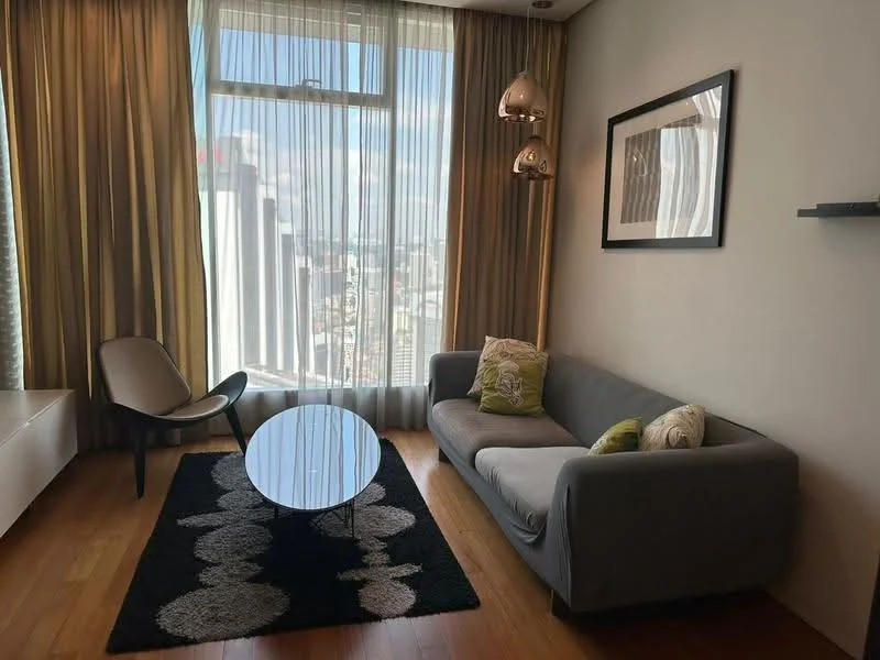 Living features: grey fabric sofa, round coffee table with black top, area rug with circular pattern, floor-to-ceiling windows, sheer curtains, wooden flooring, two pendant lights, decorative wall art, wall-mounted shelf; style: modern; view: city.