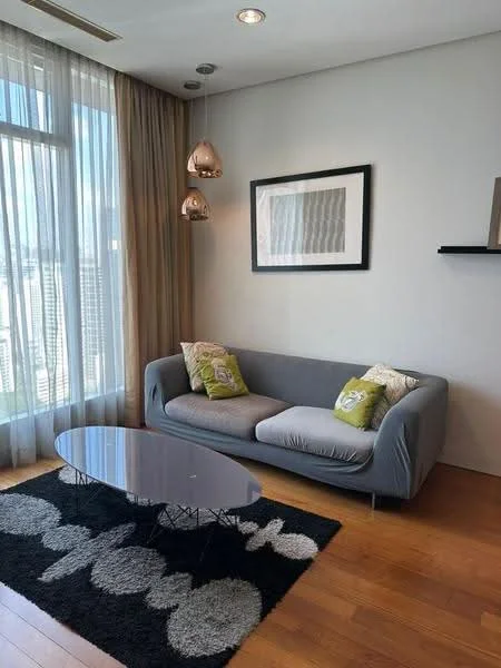 Living features: 3-seater fabric sofa in grey, decorative cushions in green, glass coffee table with round top, area rug with floral pattern, floor-to-ceiling windows, sheer curtains, wooden flooring, 2 pendant lights, framed artwork on wall, wall-mounted shelf; style: modern; view: city.