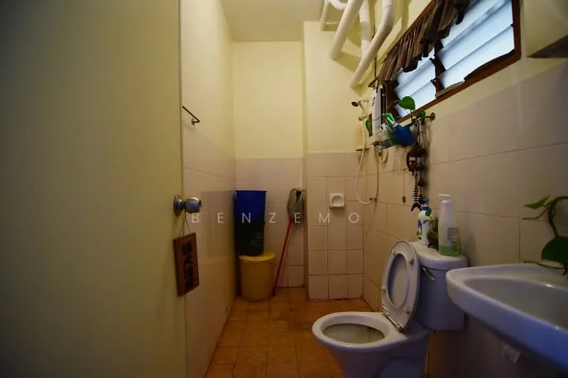 Bathroom features: white toilet, sink with chrome faucet, tile flooring, white tiled walls, window with blinds, greenery on windowsill, cleaning supplies visible, yellow bucket, shower hose, wall-mounted mirror.