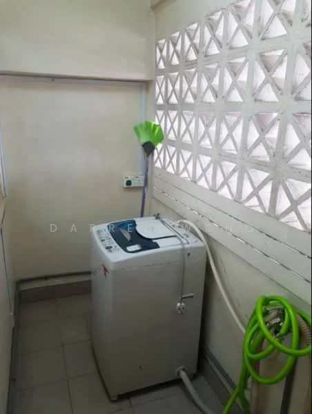 Laundry features: front-load washing machine, green hose, broom, grey tiled flooring, white walls, decorative ventilation blocks, window for natural light.