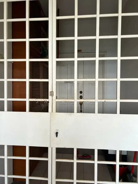 Room features: white metal security grille door, white painted walls, white tiled flooring, wooden storage cabinets, door with doorknob and lock, light switch, visible floor mat.