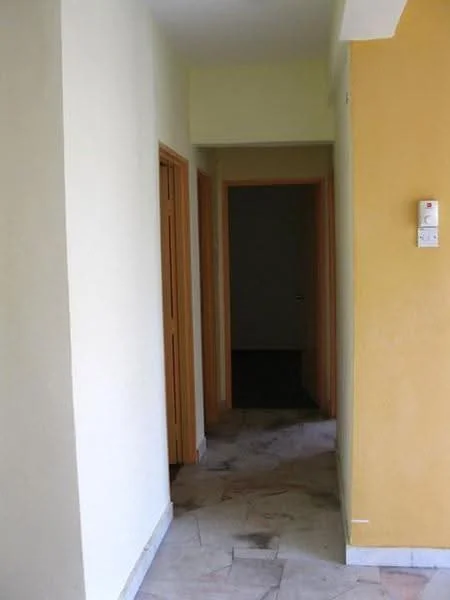 Hallway features: yellow painted walls, light cream painted walls, marble tile flooring, wooden doors, door frames, light switch, open doorway, neutral lighting.