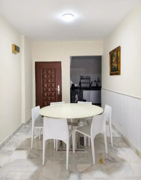 Dining features: round dining table with marble top, 4 white plastic dining chairs, cream painted walls, marble flooring, recessed ceiling light, wooden door with decorative panel, framed artwork on wall, wainscoting along the lower wall; style: modern.