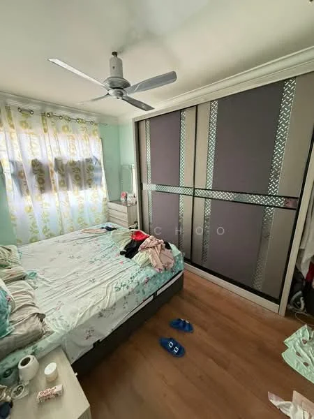 Bedroom features: queen-size bed with floral bedding, wooden flooring, 5-blade ceiling fan, built-in wardrobe with sliding doors, curtains with floral pattern, nightstand, decorative wall paneling, clothes on bed, slippers on floor.