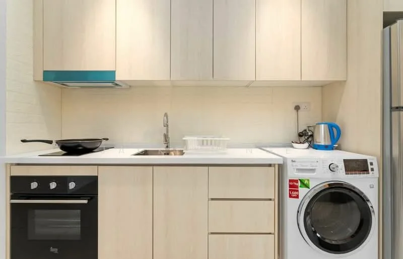 Kitchen features: light wood cabinetry, white countertop, single-bowl stainless-steel sink, chrome pull-down faucet, built-in oven, 4-burner gas hob, stainless-steel range hood, front-load washing machine, kettle, frying pan, wall-mounted electrical outlet, white tiled backsplash; style: modern.
