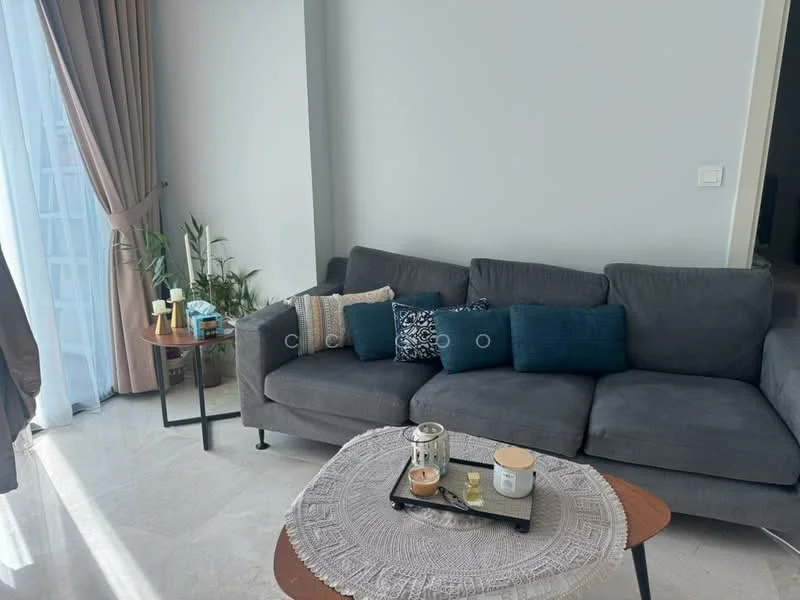 Living features: grey fabric sectional sofa, decorative cushions in various colors, round coffee table with woven placemat, glass candle holder, small decorative items on the table, floor-to-ceiling windows with sheer curtains, indoor plants, marble flooring, light-colored painted walls; style: modern.