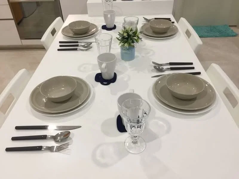 Dining features: white dining table, 6 dining chairs, beige dinner plates, beige soup bowls, clear drinking glasses, cutlery set with forks and knives, blue decorative flower vase, blue placemats; style: modern.