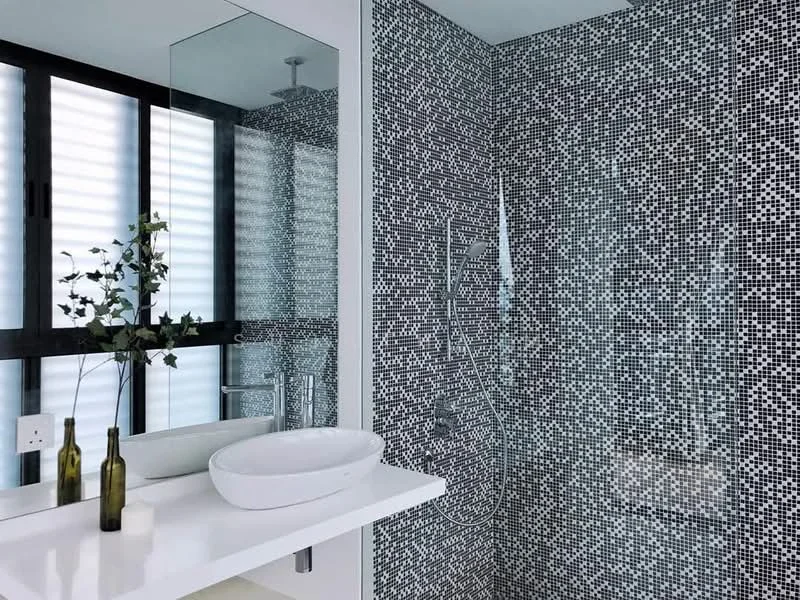 Bathroom features: mosaic tile cladding on walls, white countertop, round vessel sink, chrome basin mixer faucet, glass shower enclosure, rain shower head, wall-mounted mirror, recessed lighting, sliding glass windows, decorative plant in vase; style: modern.