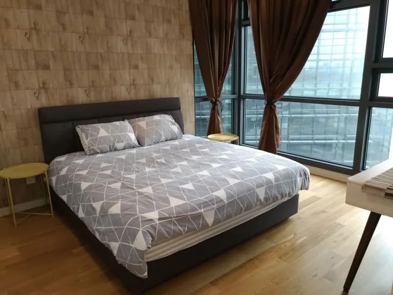 Bedroom features: queen-size bed with grey geometric patterned bedding, wooden flooring, floor-to-ceiling windows, brown curtains, two round side tables with yellow tops, decorative wall with wood paneling, wall-mounted light fixture, minimalist decor; style: modern; view: city.