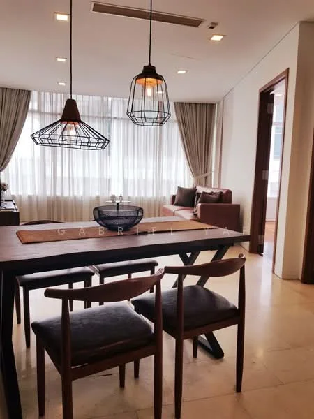 Dining features: wood dining table, 4 wooden dining chairs, pendant lighting with wire cage design, large windows with sheer curtains, cream-colored walls, marble flooring, decorative bowl on table, sofa in background, curtains in neutral color; style: modern.