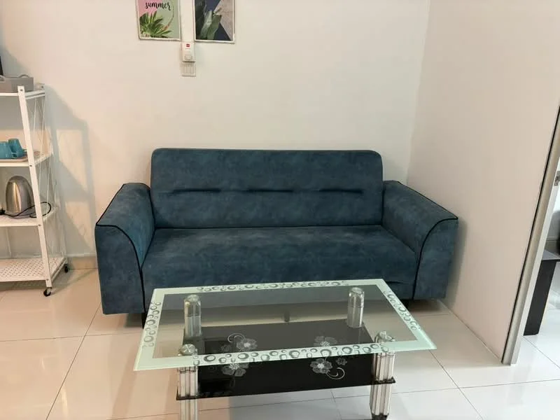 Living features: blue fabric sofa, glass coffee table with decorative design, white painted walls, glossy white tile flooring, wall-mounted light switch, shelf with kettle, minimalist decor; style: modern.