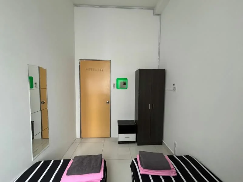 Bedroom features: two single beds with black and white striped bedding, pink towels on beds, white painted walls, tile flooring, full-length mirror, wooden door with a peephole, dark wood wardrobe, small bedside table, green wall-mounted decor, window with no visible treatment; style: minimalist.