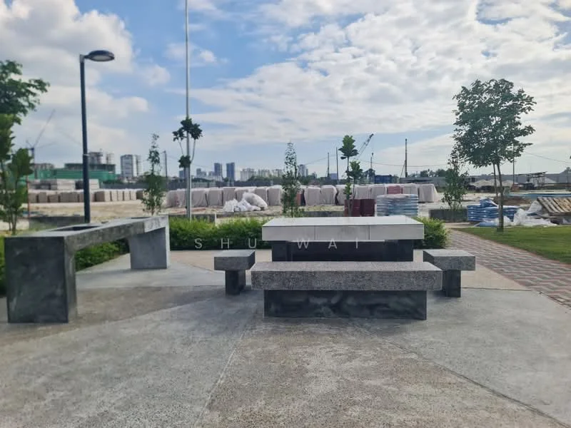 Exterior type: landscape garden; features: concrete picnic table, concrete benches, manicured lawn, paved walkway, decorative trees, urban skyline in background, construction materials stacked in background; style: modern.