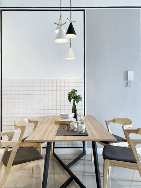Dining features: wooden dining table with black metal legs, 4 wooden dining chairs with grey upholstered seats, pendant lighting with black and white shades, white walls with black outline, grey accent wall, grid-patterned tile backsplash, decorative plant in ceramic pot, table setting with plates and cups; style: modern.
