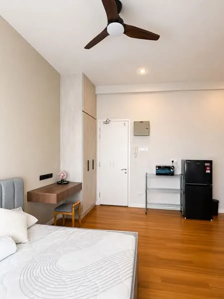 Bedroom features: queen-size bed, upholstered headboard, wooden flooring, 5-blade ceiling fan, wall-mounted light fixture, built-in wardrobe with sliding doors, study desk with chair, mini fridge, metal shelving unit, white painted walls, door with security lock, window with blinds; style: modern.