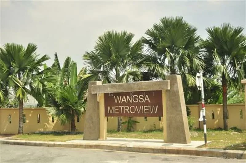 Exterior features: signage with the name 'Wangsa Metroview', tropical landscaping with palm trees, manicured lawn, yellow painted wall, stone structure supporting the sign, roadway leading to the entrance; style: modern.