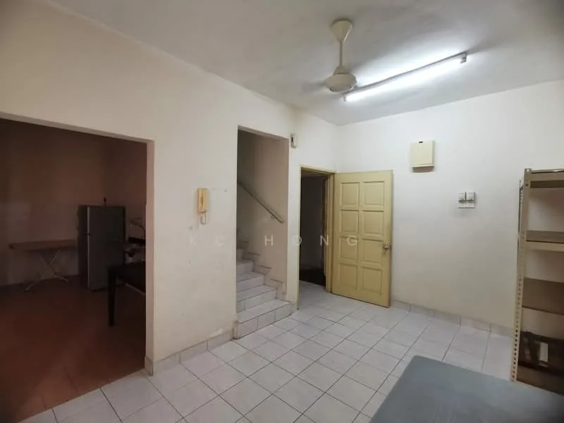 Room features: white painted walls, tiled flooring, ceiling light fixture, ceiling fan, staircase leading to upper floor, yellow door, telephone wall unit, open shelving unit, refrigerator visible in adjacent room.