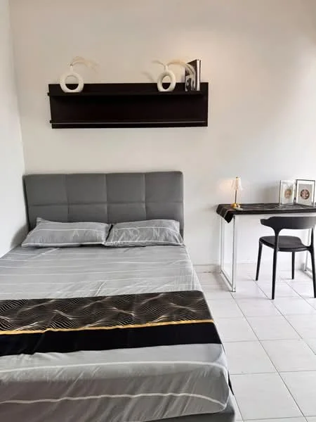 Bedroom features: queen-size bed with grey upholstered headboard, grey bedding, white walls, black accent throw, floating shelf above bed, decorative vases on shelf, small desk with white frame, black chair, table lamp on desk, tile flooring, natural light from window; style: modern.