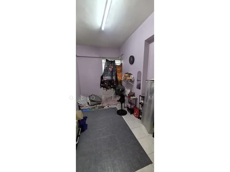 Room features: purple painted walls, vinyl flooring, ceiling lights, window with sheer curtains, standing fan, small shelf unit, refrigerator, cluttered space.