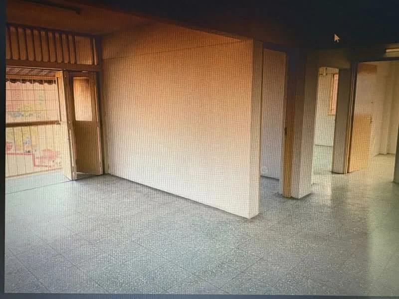 Room features: plain white walls, grey tiled flooring, door leading to outdoor area, multiple doorways, natural light from windows, open layout, no visible furniture, neutral color scheme; style: minimalist.