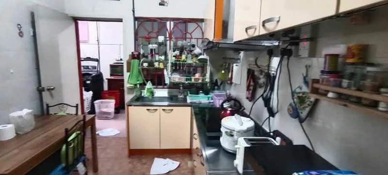 Kitchen features: black countertop, cream cabinetry, stainless-steel sink, chrome pull-down faucet, built-in stove, microwave, rice cooker, open shelving, wall-mounted storage, tile flooring, green dish towels, kitchen table with chairs, various kitchen utensils, refrigerator visible in background.