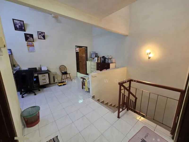 Room features: white painted walls, tile flooring, staircase with railing, wall-mounted light fixture, desk with chair, storage cabinet, framed photographs on wall, basket, open space, doorway leading to another room.