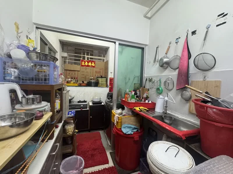 Kitchen features: red countertop, stainless-steel sink, single-bowl stainless-steel sink, kitchen cabinets, gas stove, metal pots and pans, plastic storage containers, red plastic trash bin, wooden cutting board, area rug in red, open shelving, glass door leading to outdoor area.