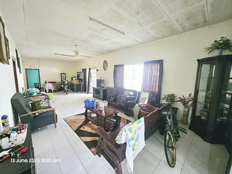 Living features: white painted walls, tile flooring, ceiling fan, large windows with sheer curtains, brown wooden coffee table, 3-seater wooden sofa, 2-seater wooden sofa, wooden display cabinet, area rug with geometric pattern, decorative plants in pots, bicycle, laundry hanging on a rack; style: traditional.