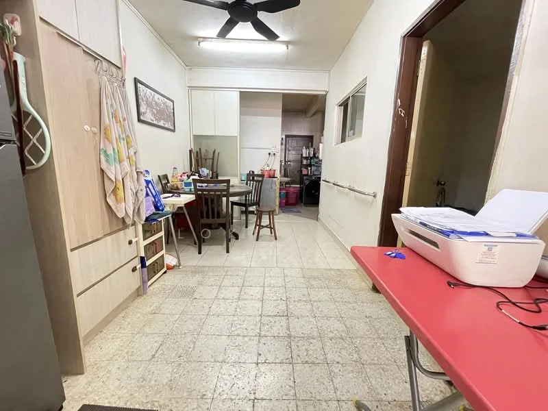 Room features: tile flooring, white painted walls, ceiling fan, wooden dining table, wooden chairs, red table, kitchen cabinetry, refrigerator, open layout, window, utility area, various kitchen items on table.