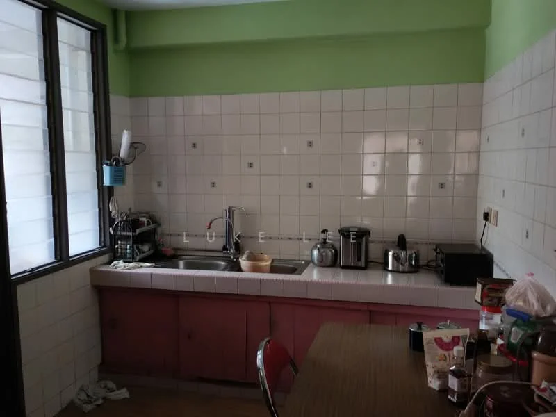 Kitchen features: green painted walls, white tiled walls, single-bowl stainless-steel sink, chrome pull-down faucet, pink cabinetry, countertop with white tiles, built-in electric kettle, freestanding toaster, freestanding rice cooker, kitchen table with chairs, window with grid pattern, flooring with wood finish.