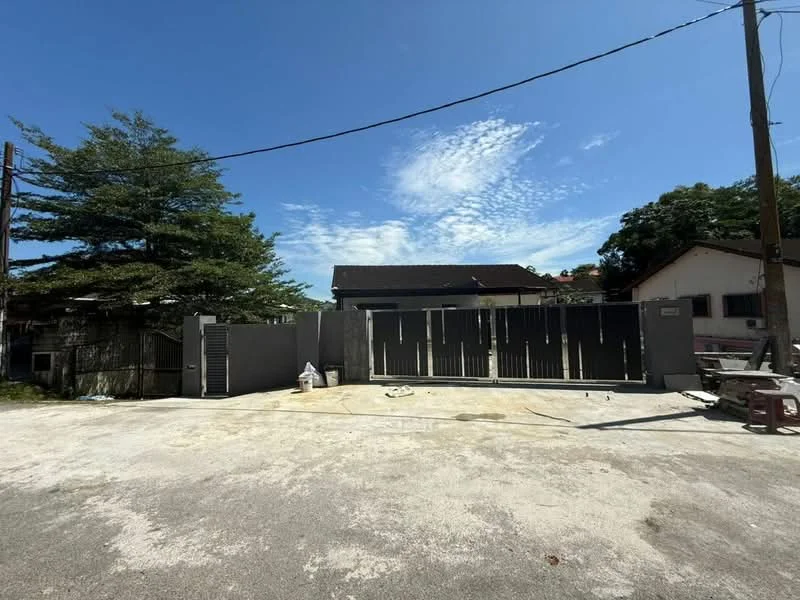 Exterior features: grey painted gate, concrete driveway, manicured trees, clear blue sky, single-storey building in background, fencing around property, power lines visible; style: modern.