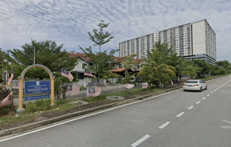 Exterior type: low-rise apartment block; features: signage at entrance, roadside with markings, palm trees, manicured landscaping, multiple flags, adjacent residential houses, multi-storey building in background, urban setting; style: modern.