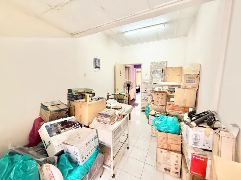 Room features: white painted walls, glossy white tile flooring, ceiling fan, various cardboard boxes, plastic bags, metal shelving unit, bed frame, stacked items, cluttered space.