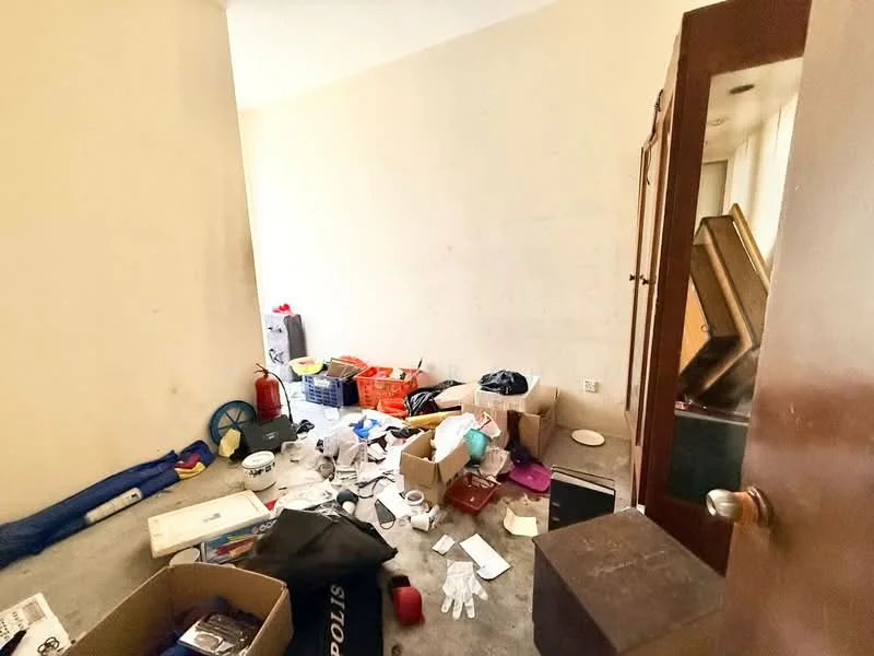 Room features: light beige painted walls, concrete flooring, cluttered with boxes, various household items scattered, plastic containers, cardboard boxes, cleaning supplies, metallic object, door partially open.