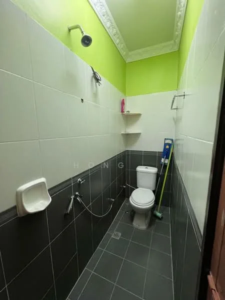 Bathroom features: green painted walls, white tiled walls, black tiled flooring, one-piece toilet, urinal, shower head, wall-mounted shelf, cleaning supplies, mop, floor drain.