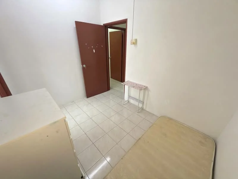 Room features: white painted walls, white tiled flooring, single bed frame without mattress, small side table, brown wooden door, light switch, doorway leading to another room.