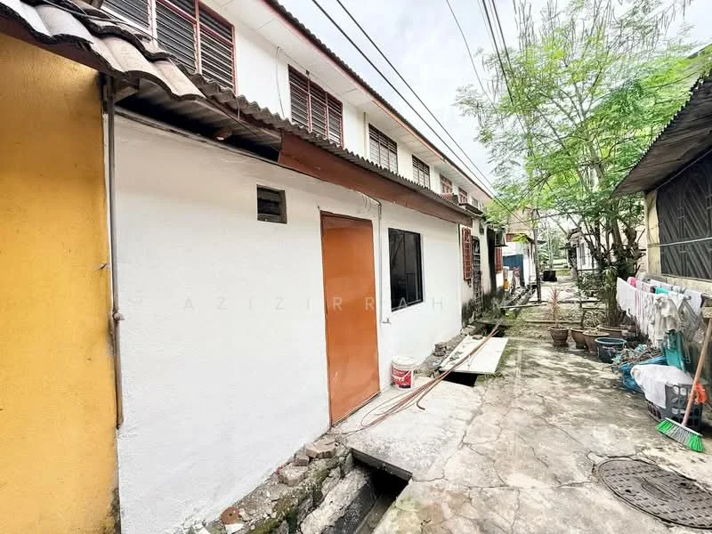 Exterior features: white painted facade, single-storey building, exposed concrete flooring, wooden door, windows with metal grilles, surrounding greenery, paved walkway, laundry area with hanging clothes.