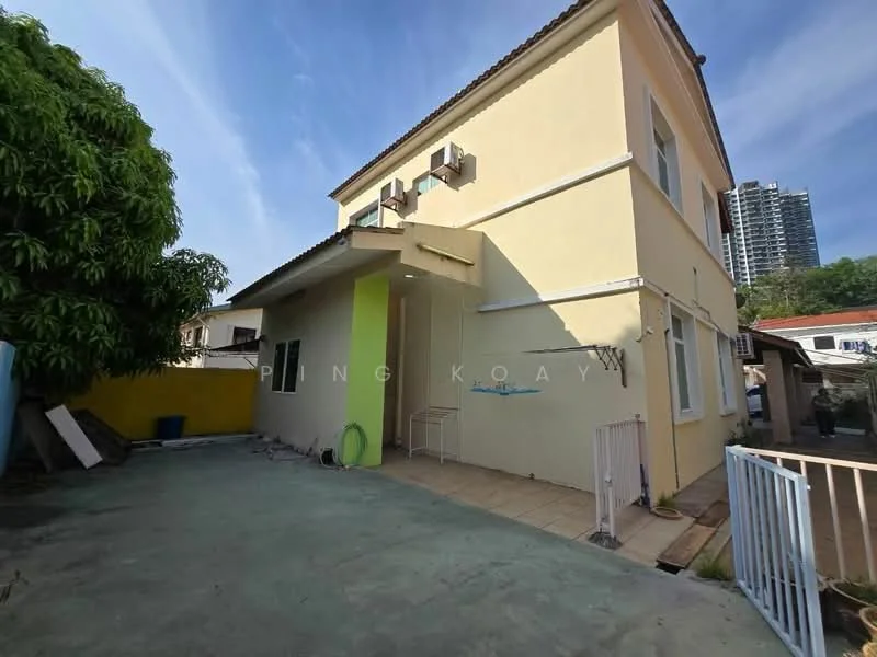Exterior type: detached bungalow; features: yellow painted facade, flat roof, 2 wall-mounted split AC units, tiled patio area, manicured lawn, surrounded by greenery, fenced yard, driveway, adjacent to high-rise buildings; style: modern.