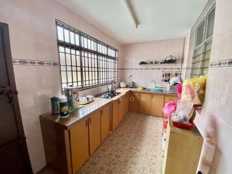Kitchen features: brown wooden cabinetry, pink tiled walls, brown countertop, gas stove with 4 burners, stainless-steel kettle, white ceramic sink, chrome faucet, window with metal grille, tile flooring, open shelving, various kitchen utensils, plastic storage containers, dish rack.