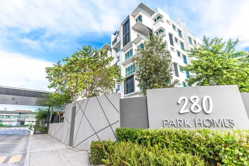 Exterior type: low-rise apartment block; features: white painted facade, glass windows, green landscaping with shrubs, manicured lawn, trees surrounding the building, modern architectural design, signage with '280 PARK HOMES', paved driveway, covered entrance, balconies on upper floors; style: modern.