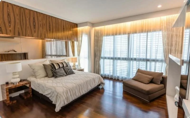 Bedroom features: king-size bed with upholstered headboard, decorative throw pillows, wooden bedside tables, table lamps with white shades, large windows with sheer curtains, dark wood flooring, built-in wardrobe with mirrored doors, accent wall with wood paneling, recessed lighting, floor-to-ceiling windows; style: modern; view: city.