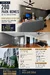 Living features: grey painted walls, wood flooring, 5-blade ceiling fan with light, wall-mounted TV, sofa in dark color, coffee table, area rug, large windows with natural light, decorative wall art; style: modern.