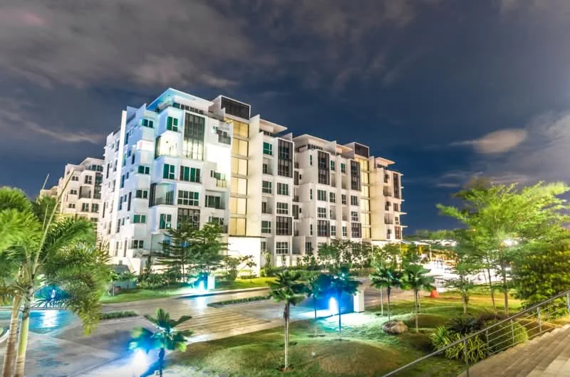 Exterior type: mid-rise condominium; features: white painted facade, glass curtain wall, recessed balconies, landscaped garden with palm trees, manicured lawn, outdoor lighting, multiple storeys, surrounded by greenery; style: modern.